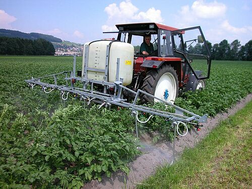 Traktor mit aufgesattelter Feldspritze im Einsatz im Kartoffelfeld