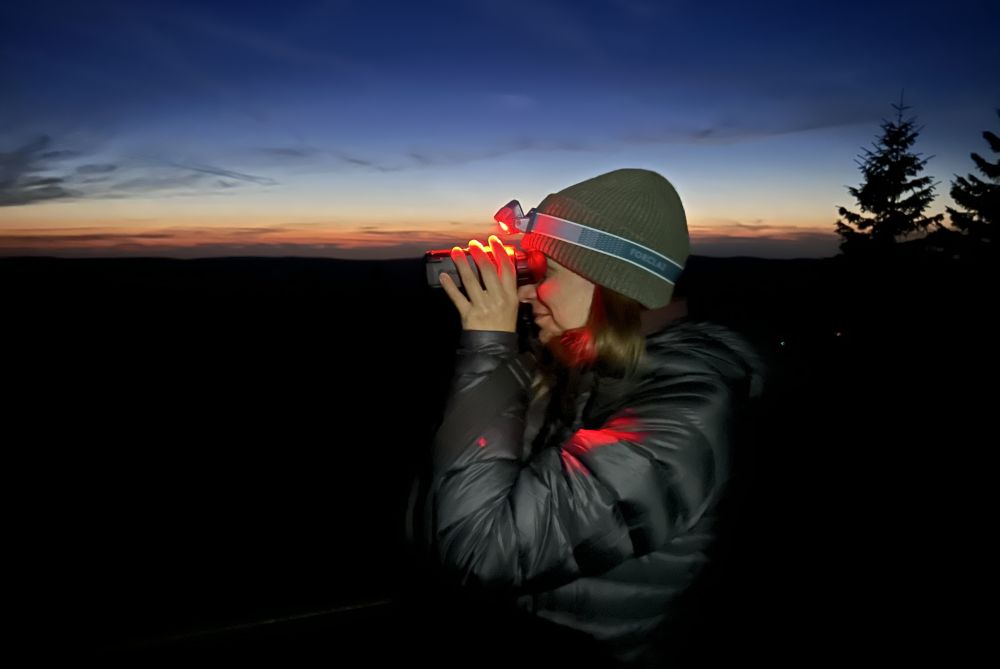Alice Dind schaut mit einem rot leuchtenden Wärmebildfernglas in die Ferne.